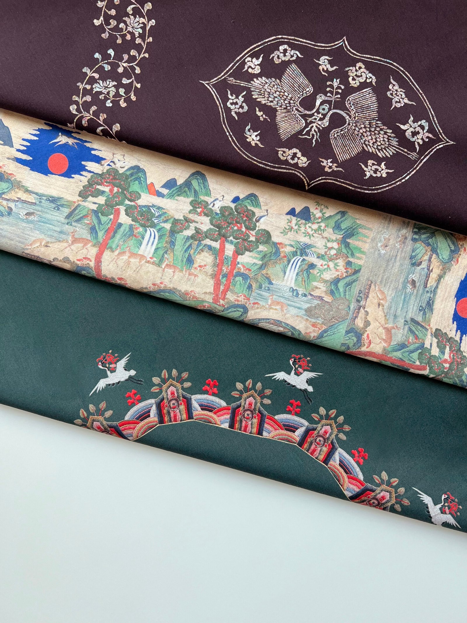 Range of bojagi from The Bojagi with Seasons layered together, showing mother-of-pearl crane, landscape, and rank badge motifs